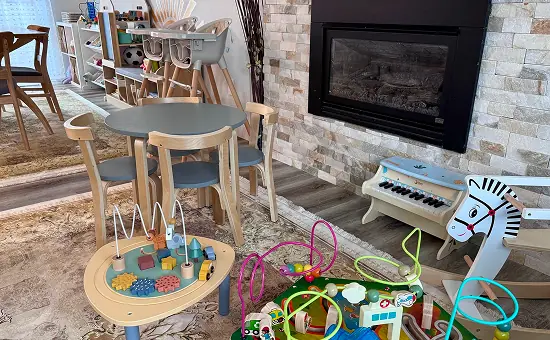 The Kido Heaven playroom: a toddler table, ride-on toys and a toy piano by the fireplace