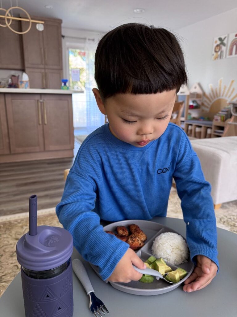 Child using child-safe utensils to foster independence at mealtime in Kido Heaven Child Care, Bothell, WA.