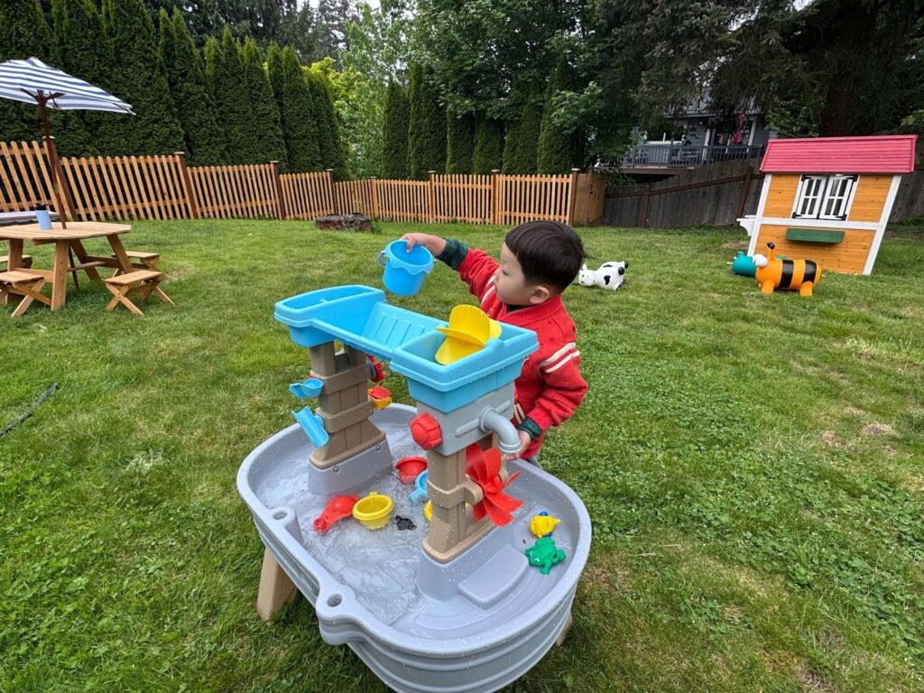 Preschoolers at Kido Heaven Child Care in Bothell, WA, pour water using containers in an outdoor STEM water play activity, fostering science inquiry and sensory development.