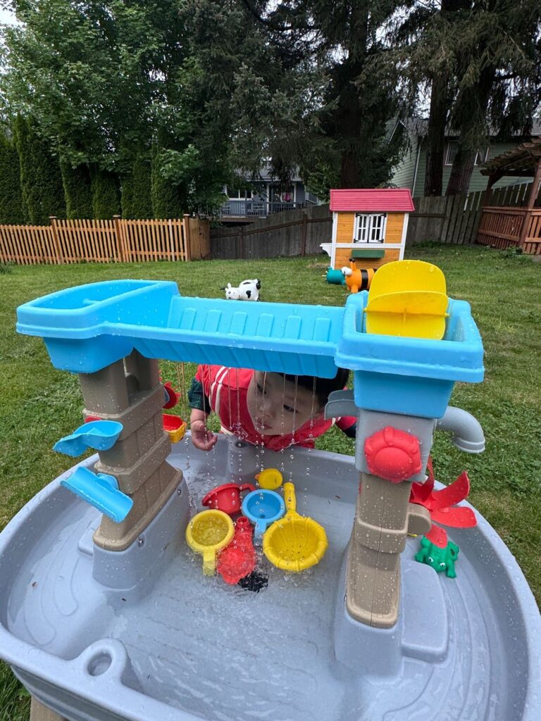 A toddler at Kido Heaven Child Care in Bothell, WA, explores water play tools in a Montessori-inspired STEM session, enhancing motor skills and curiosity.
