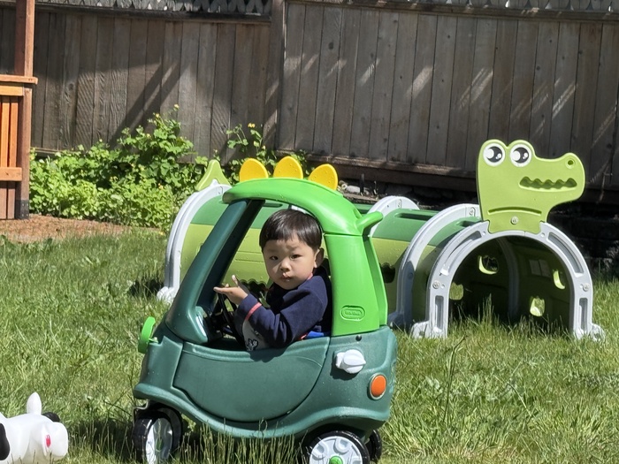 A young child playing in a green toy car outside at KidoHeaven daycare in Bothell