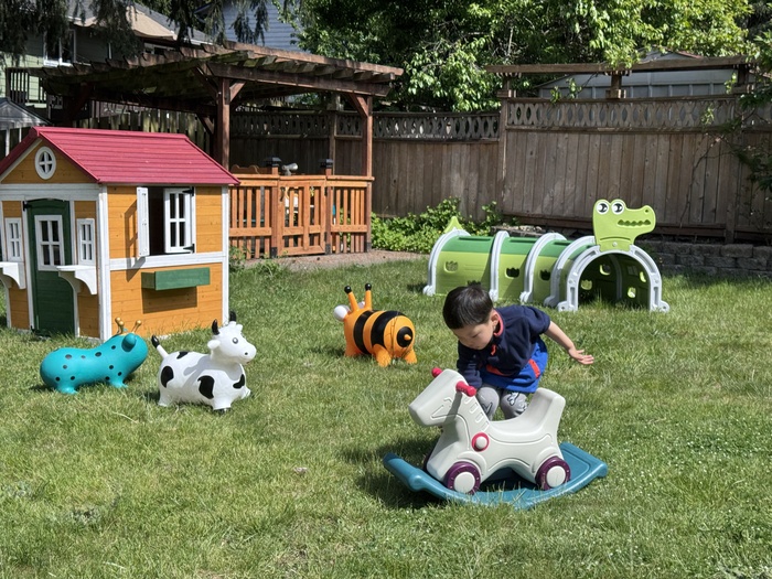 A young child joyfully engaging with a colorful push-along toy in a grassy daycare outdoor play area.  